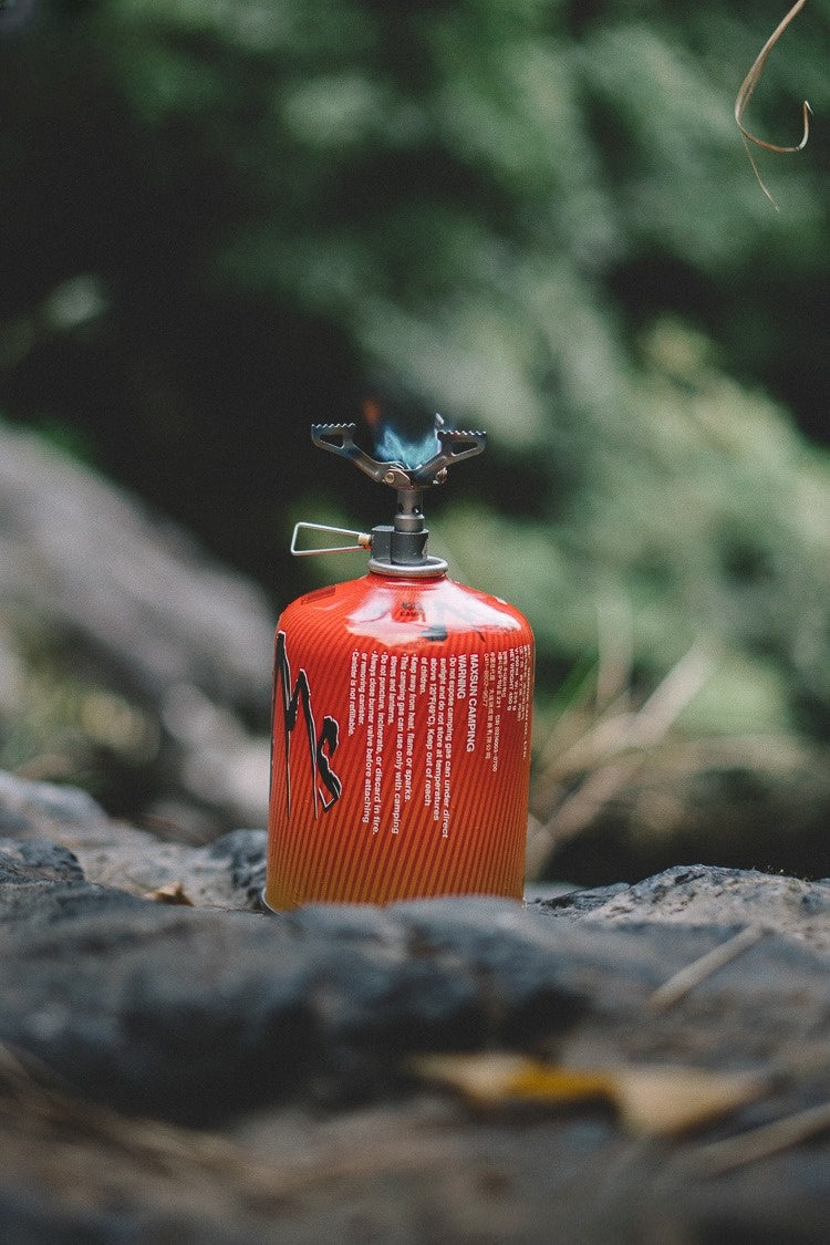 Red canister with stove head on a rock with a blurred green background