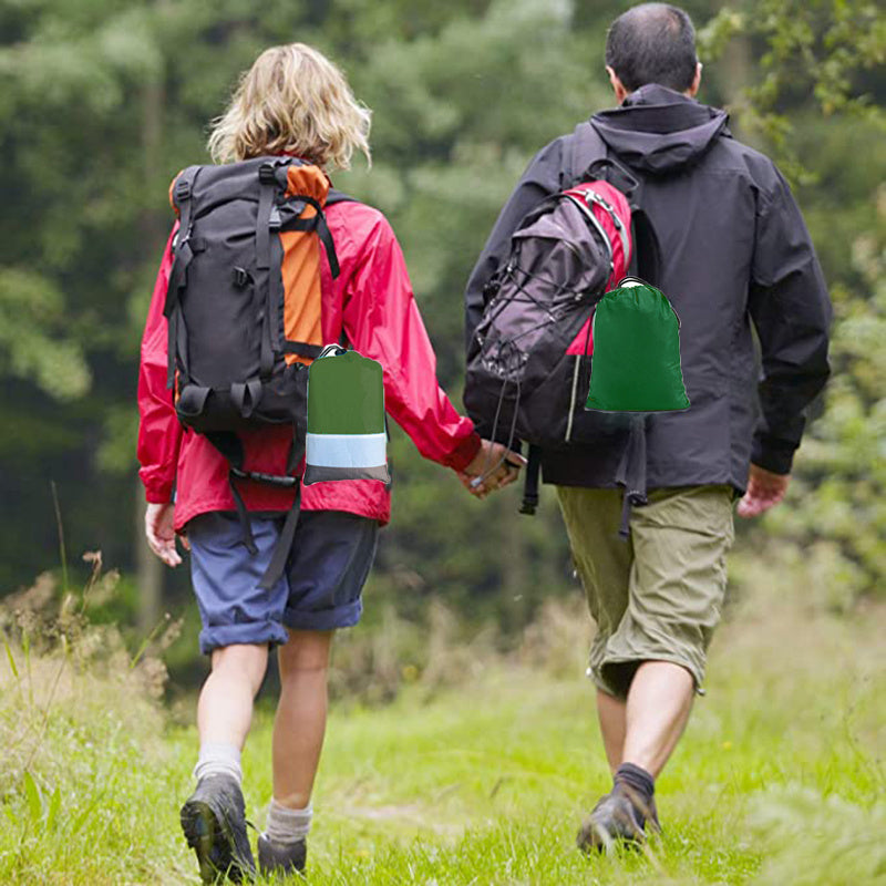Two people hiking in a forest, holding hands and carrying ultralight double hammock. 
