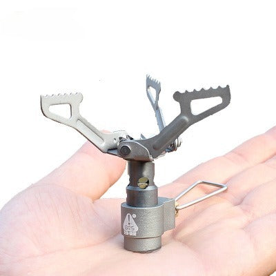 Compact camping stove head held in a hand against a white background