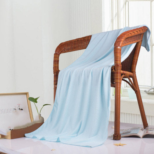 Light blue bath towel draped over a wicker chair in a room with a window and plant.