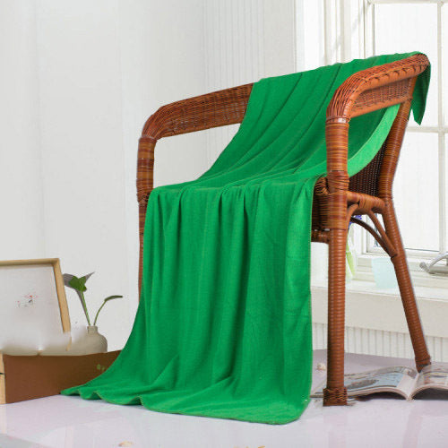 Green bath towel draped over a wicker chair in a room with a window and plant.